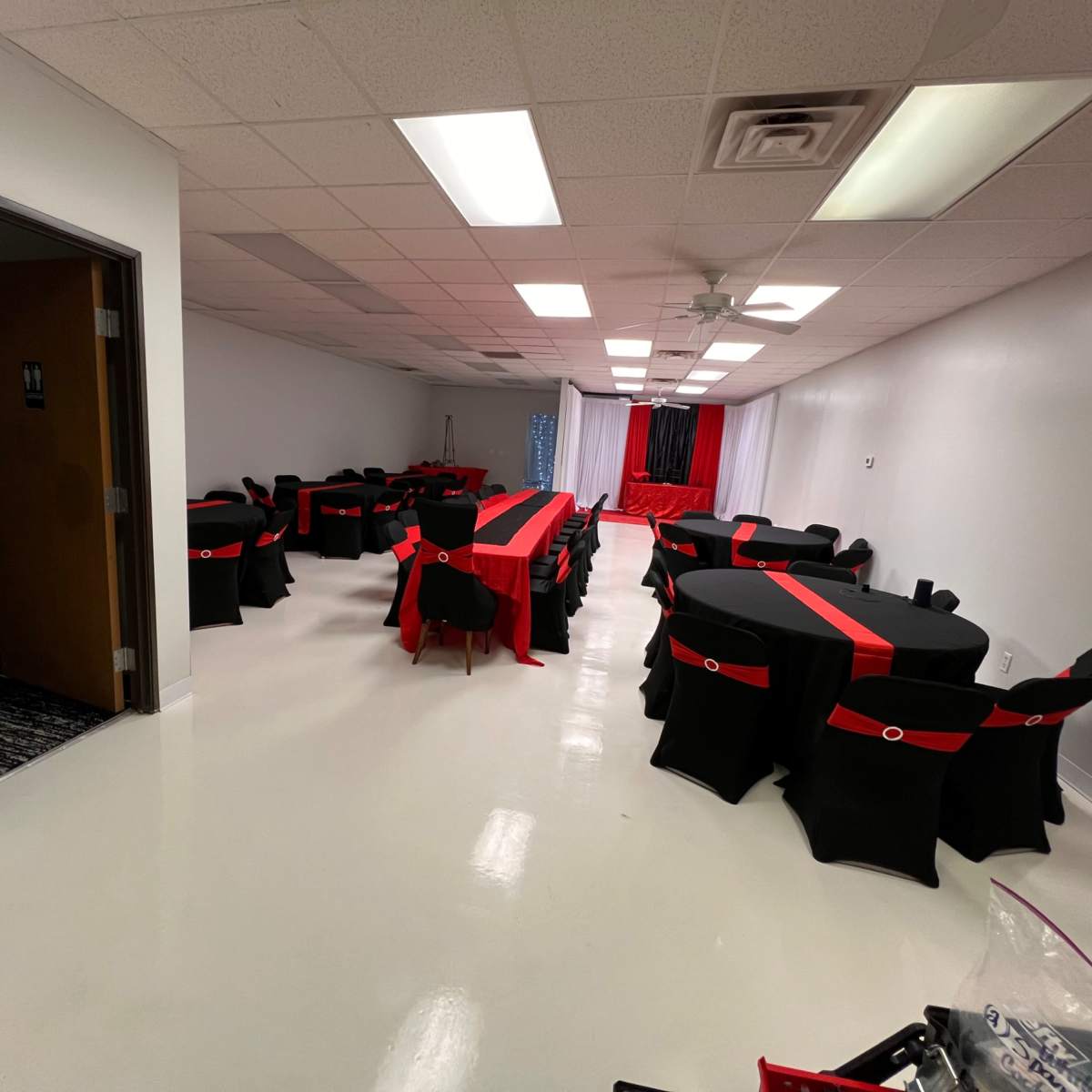 A banquet room with multiple black tables covered in red tablecloths, arranged in a symmetrical layout.