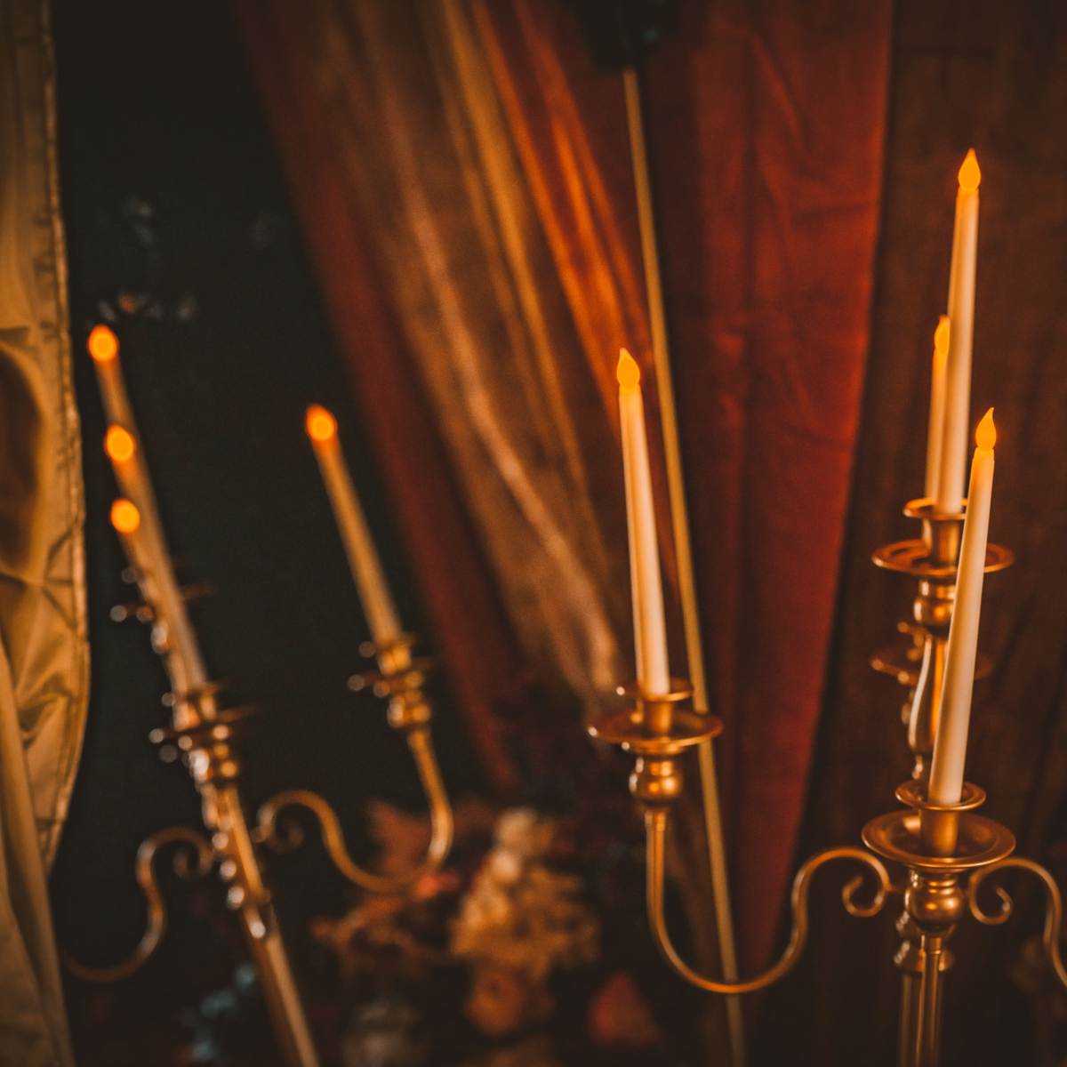 Several gold candlesticks with lit white candles arranged against a dark backdrop.