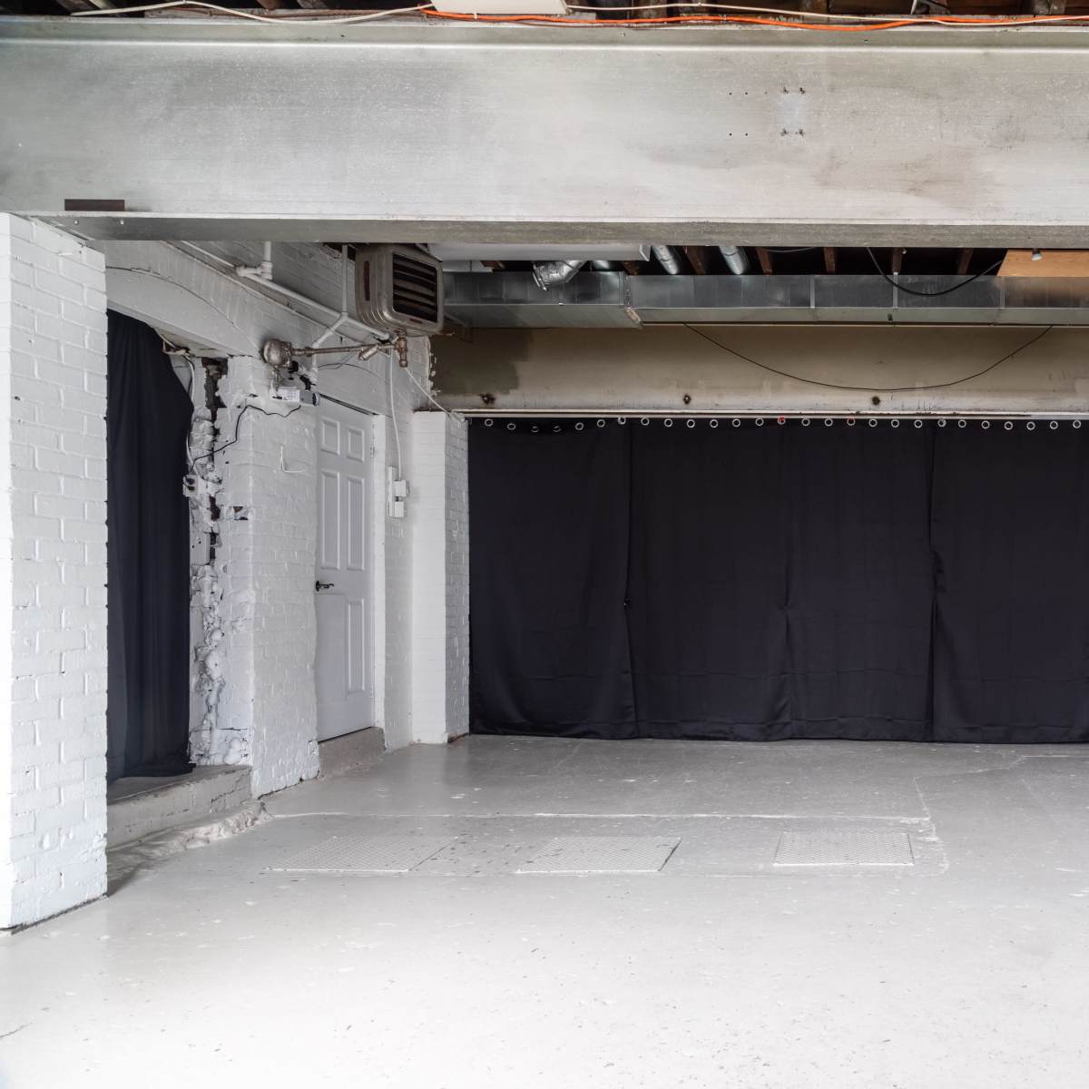 A spacious, empty room with concrete walls and a black curtain hanging across one side.