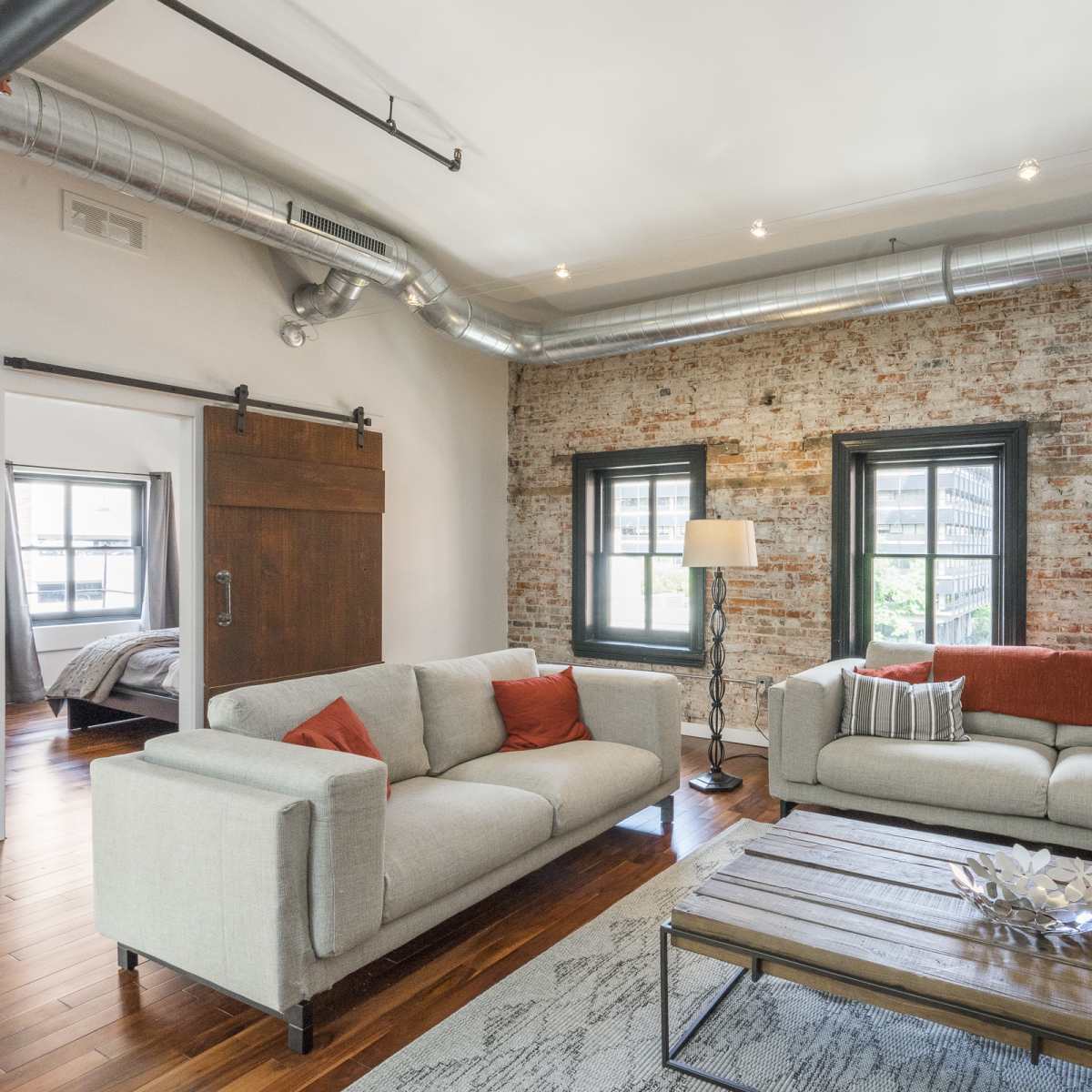 A modern living room with exposed brick walls, large windows, and a wooden coffee table between two sofas.