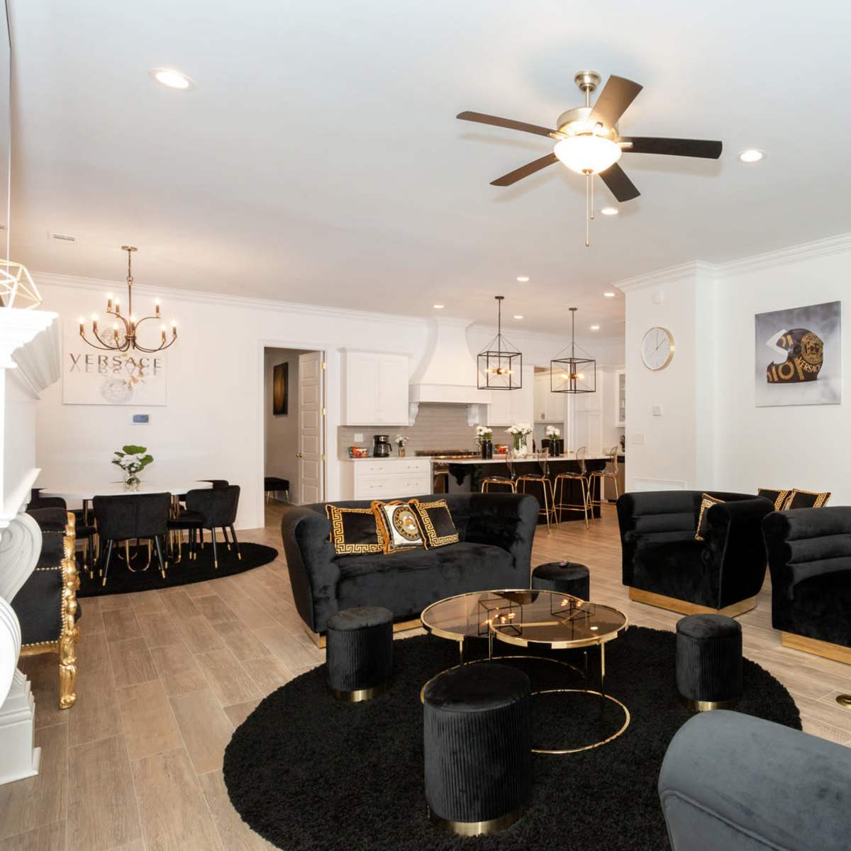 A modern living room featuring black upholstered furniture, a circular black rug, a glass coffee table, and a staircase leading to an upper floor.