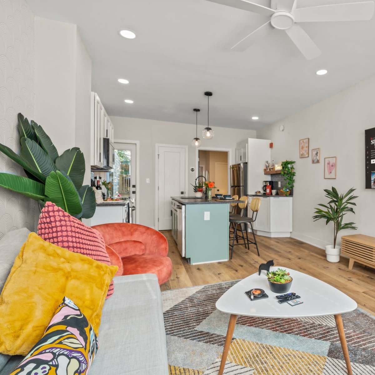 A modern living room with a light color palette, featuring a gray sofa, a wooden coffee table, a large TV mounted on the wall, and a cozy dining area in the background.