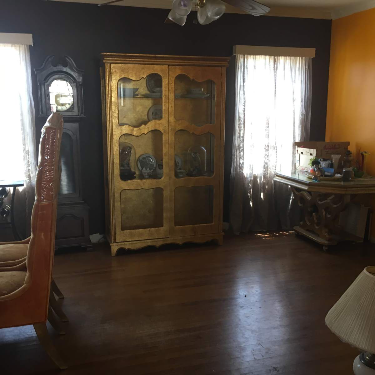 The room features a dining area with a wooden table and orange walls, complemented by a golden cabinet and a vintage clock.