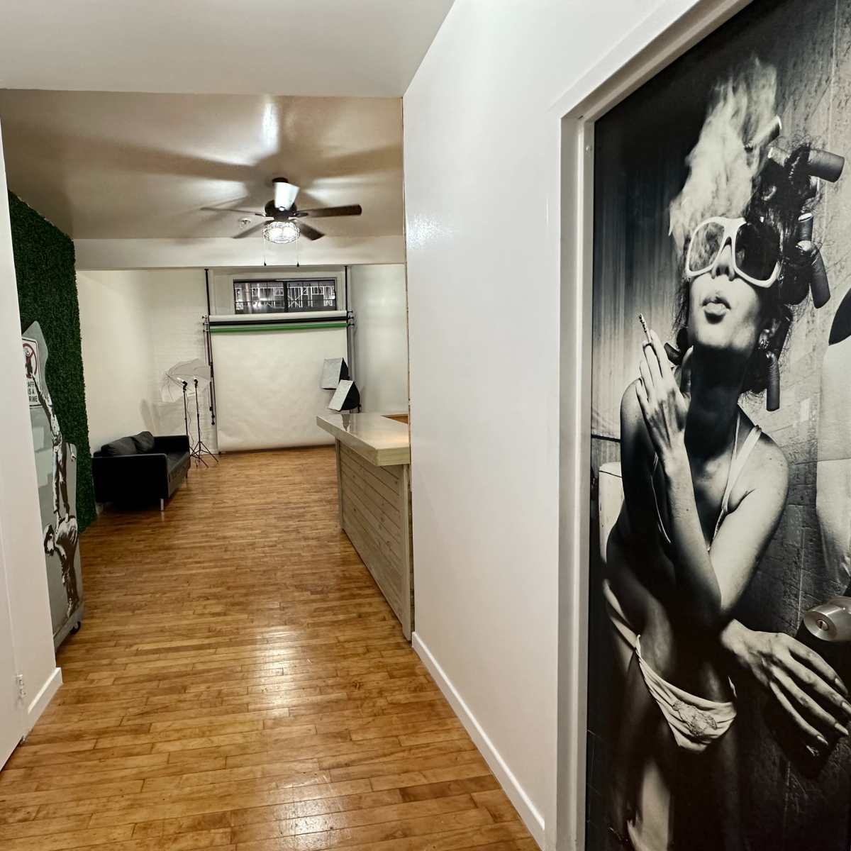 A hallway leading to a room with wooden flooring, a ceiling fan, and a black-and-white photographic mural on the door.