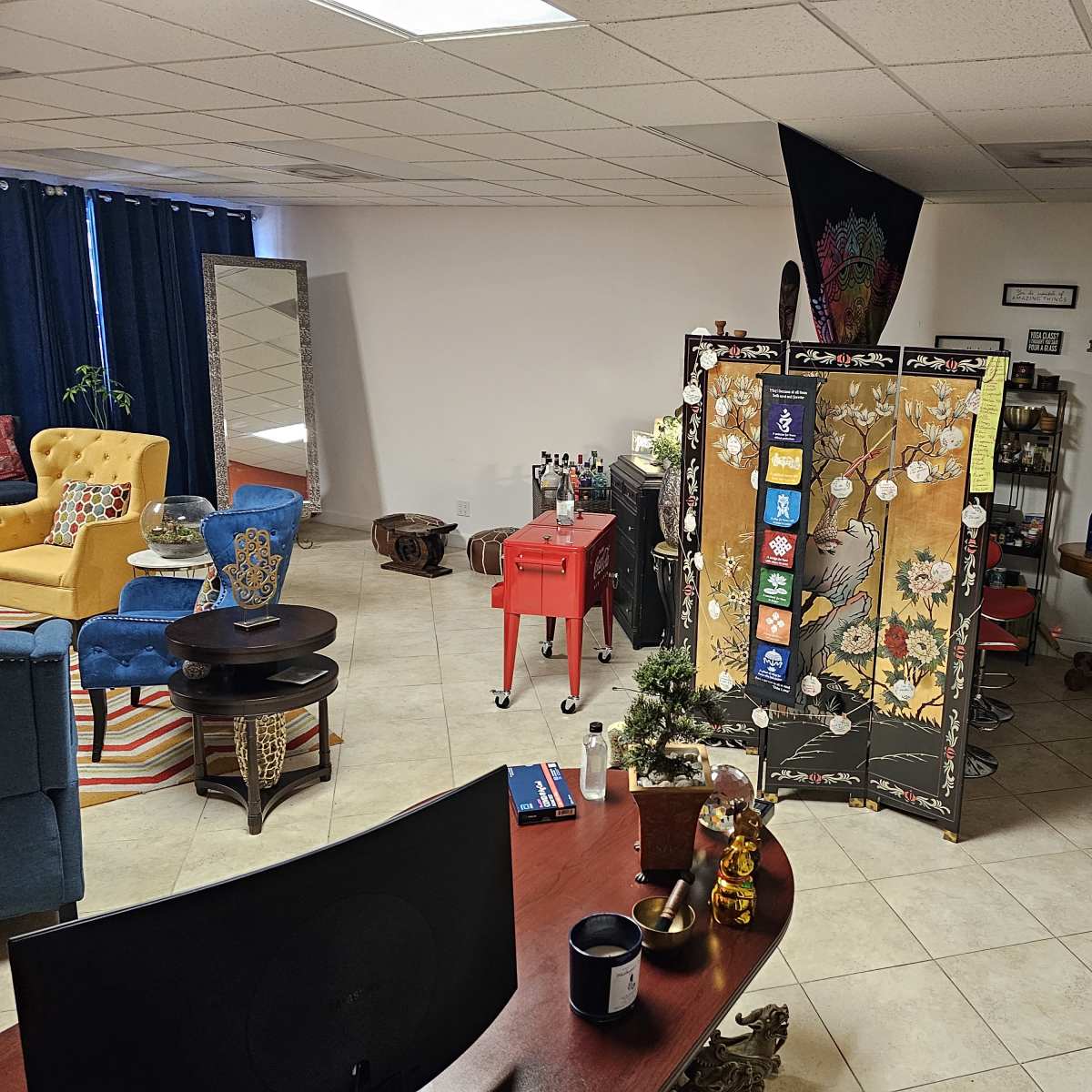A spacious and colorful lounge area with various seating options, a decorative screen, and a bar setup in a well-lit room.