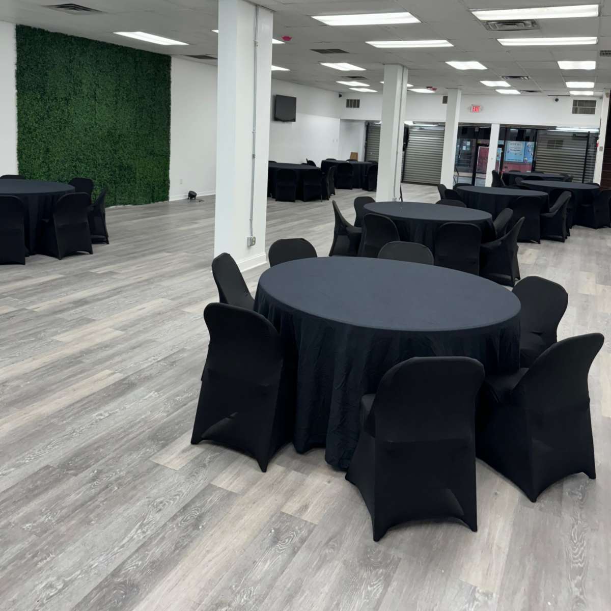 A spacious event room with several round tables covered in black tablecloths and a decorative green wall in the background.
