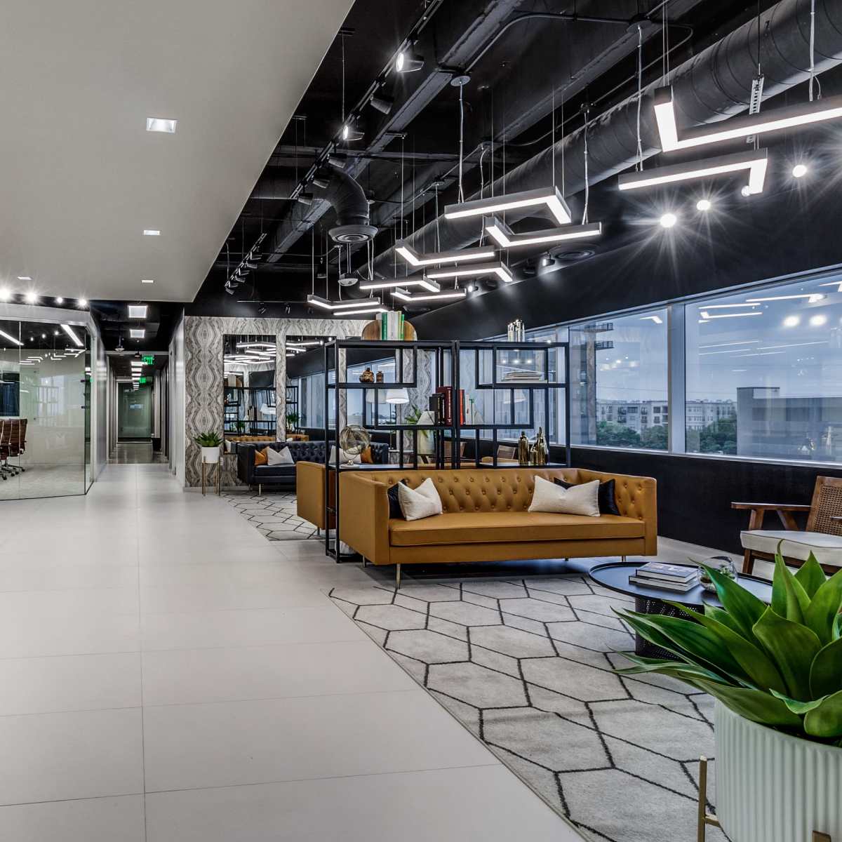 A modern office interior with a mix of seating areas, glass-walled meeting rooms, and geometric floor tiles.