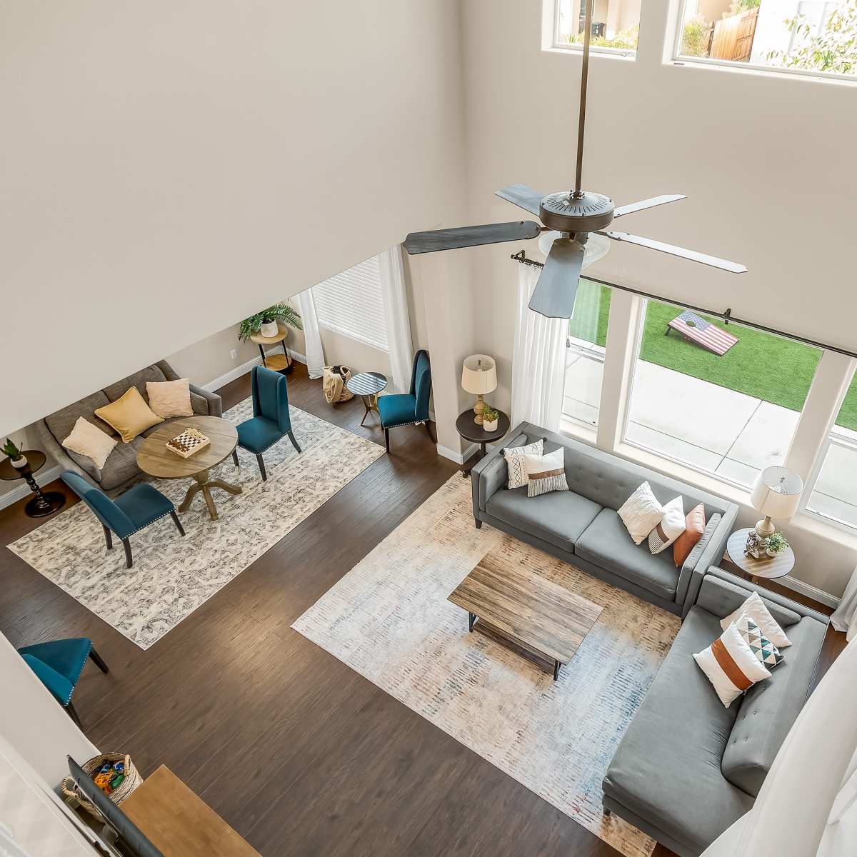 A spacious living area with a high ceiling, featuring a gray sofa, a wooden coffee table, a dining table with blue chairs, and large windows allowing natural light.