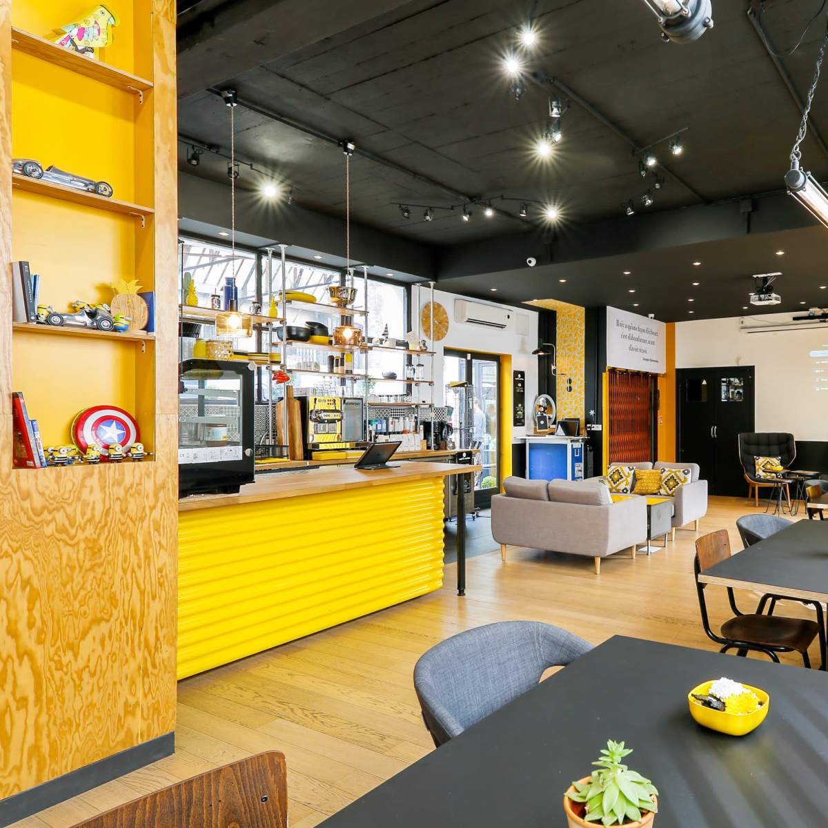 A modern café with yellow and wood accents, featuring seating areas, a coffee counter, and decorative shelves.