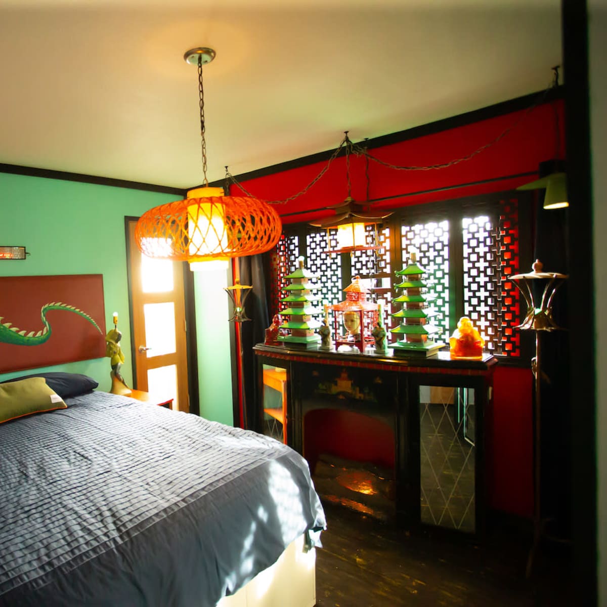 A brightly colored bedroom featuring a large bed, a decorative dragon mural, and a distinctive lamp above.