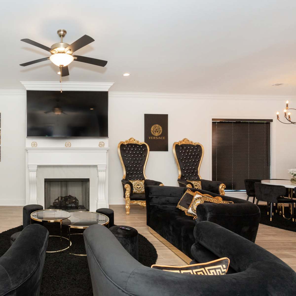 A modern living room featuring black velvet sofas with gold accents, a fireplace, a large wall-mounted television, and elegant decorative elements.