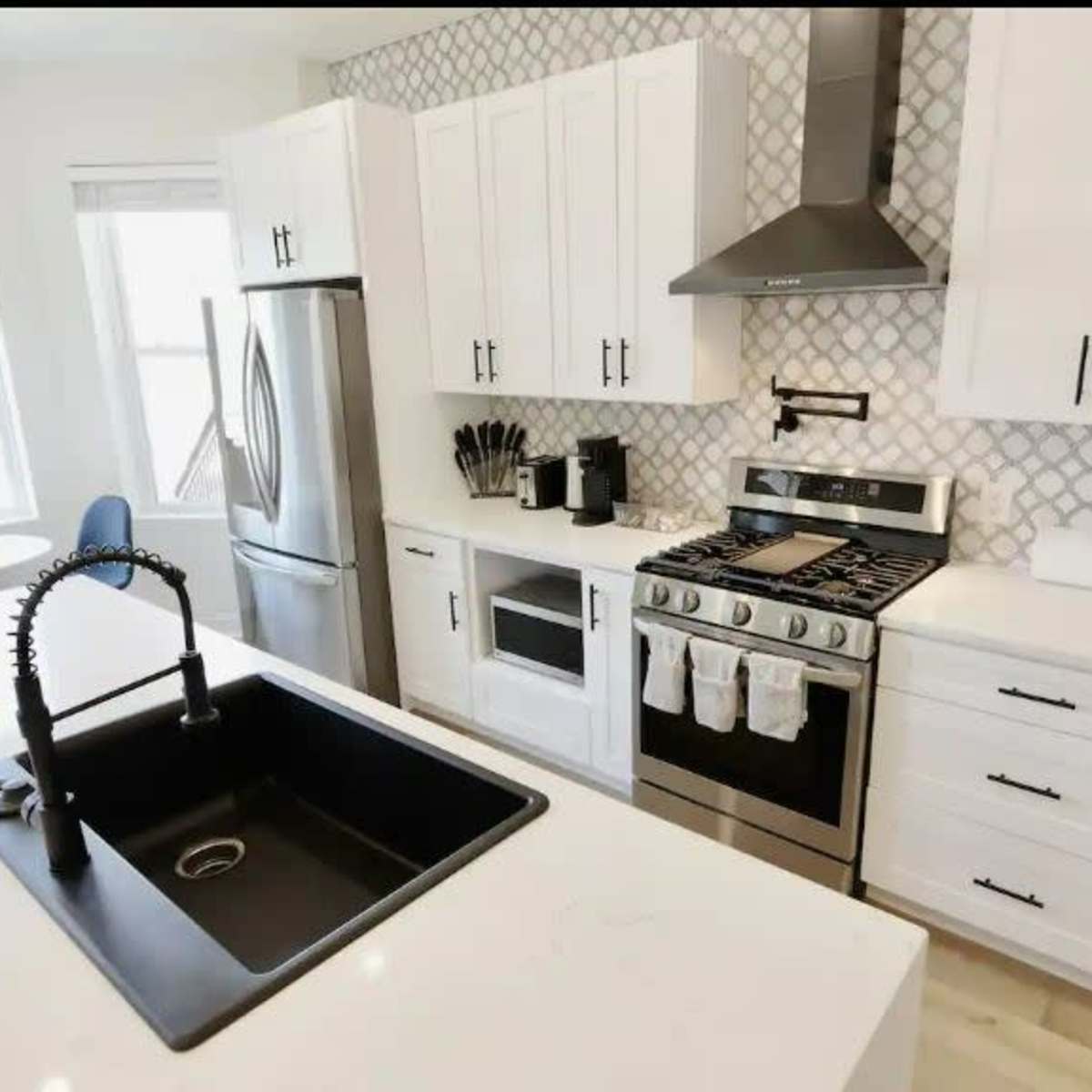 The modern kitchen features white cabinets, a stainless steel refrigerator, a black sink, and a gas stove with a decorative backsplash.