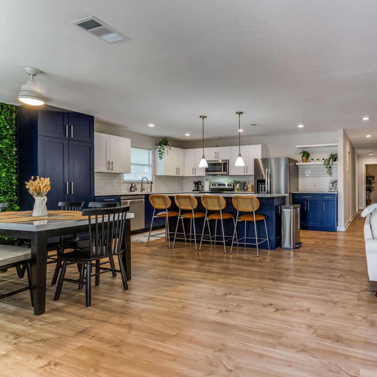 A modern open-concept kitchen and living area with dark blue cabinets, wooden flooring, and various indoor plants.