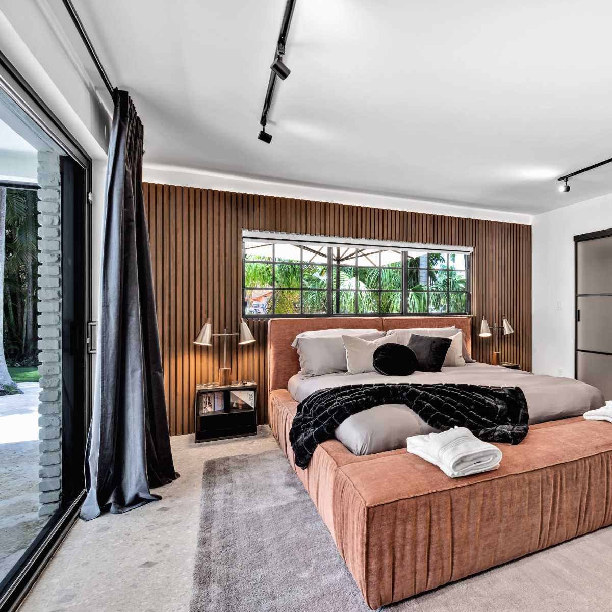 A modern bedroom with a large bed, wooden accent wall, and sliding glass doors opening to an outdoor space.
