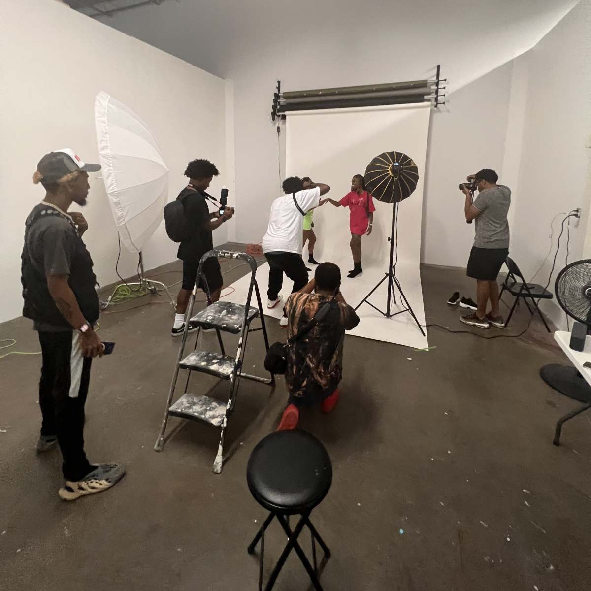 A group of people are engaged in a photoshoot in a studio, with lighting equipment and a backdrop set up for the session.