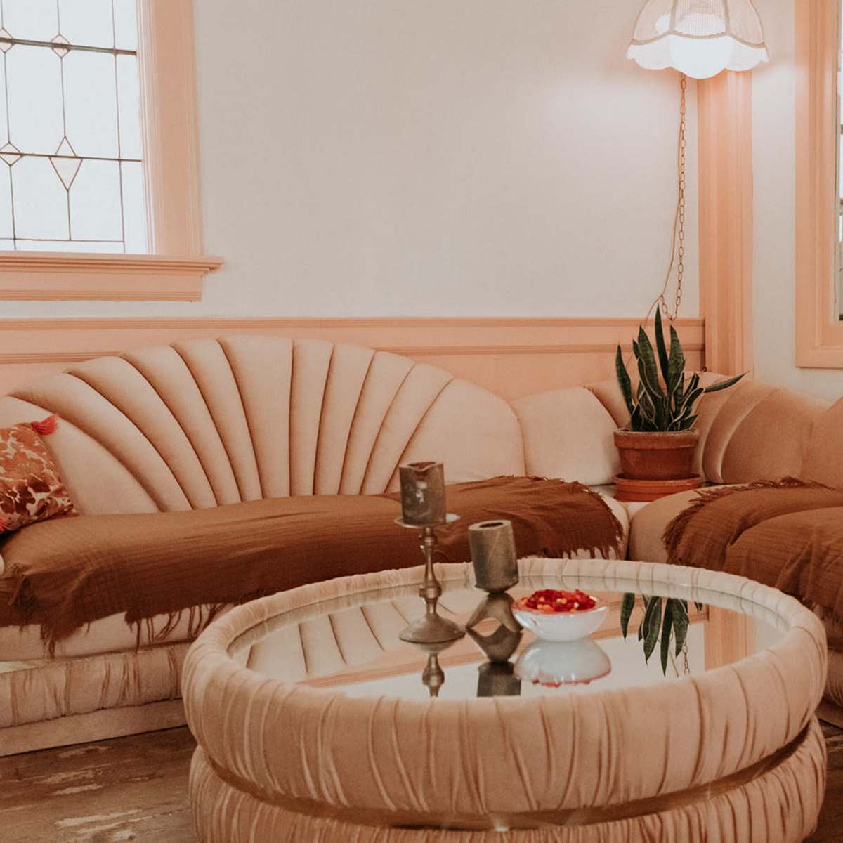 A cozy living room with two curved, upholstered sofas, a round glass coffee table, and a potted plant.
