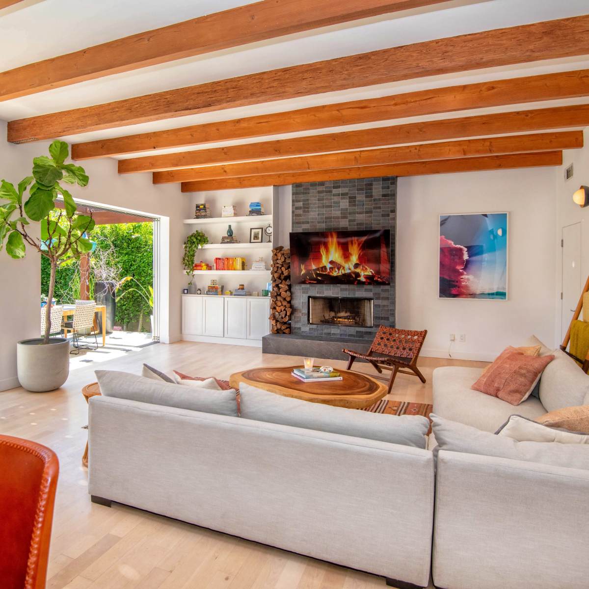 A modern living room with wooden beams, a fireplace, and large open doors leading to a garden.