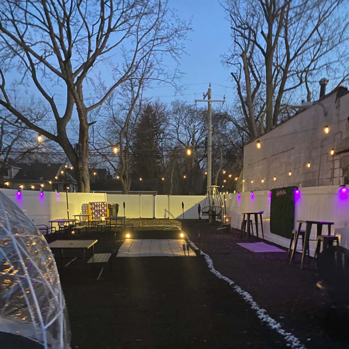 A landscaped outdoor area with tables, string lights, and a pathway leading through a garden space during dusk.
