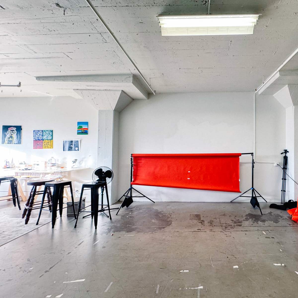 A spacious room with a red photographic backdrop on stands, a table with chairs, a fan, and a yellow object on the floor.