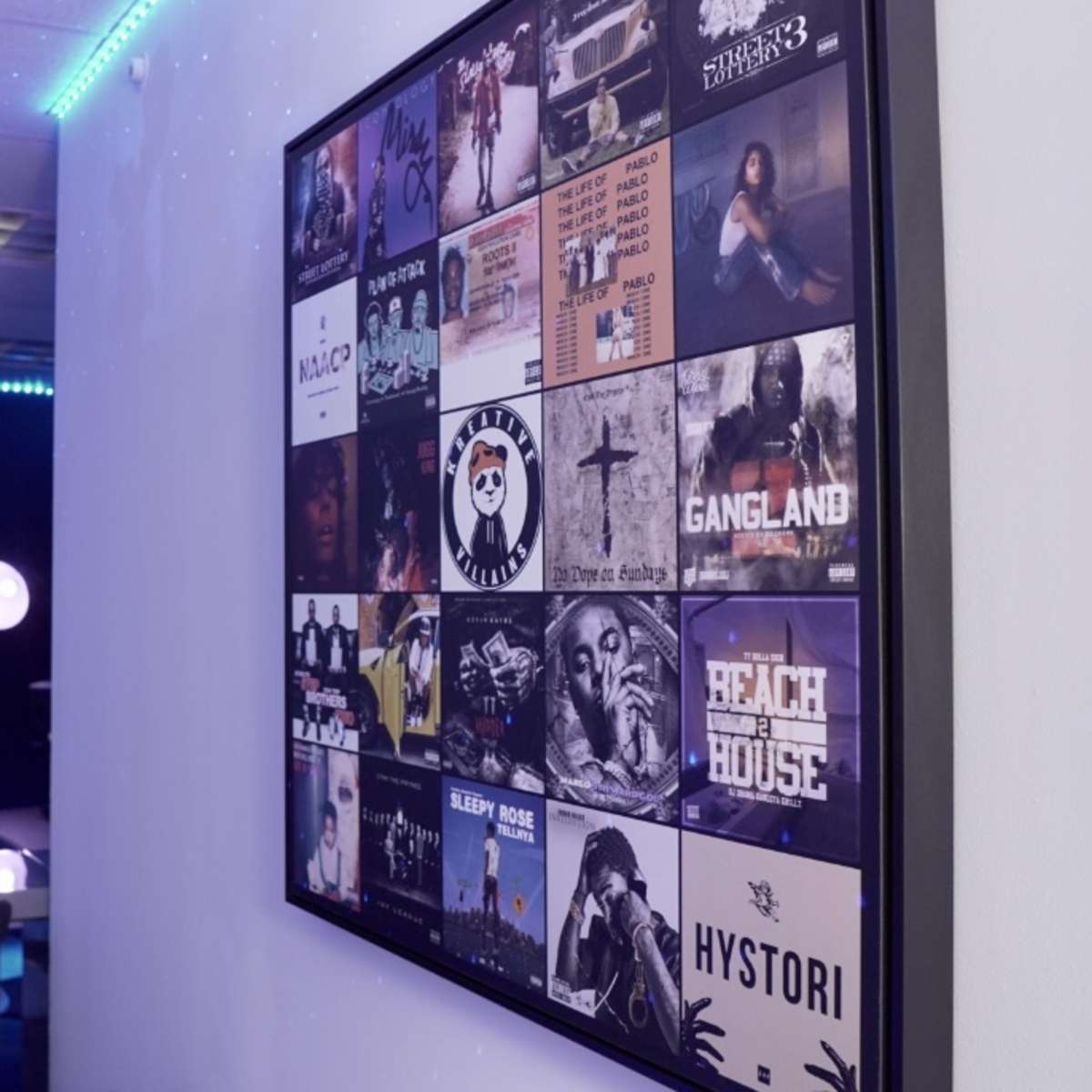 A wall-mounted collage of album covers beside a table and chairs with a computer setup in a dimly lit room.