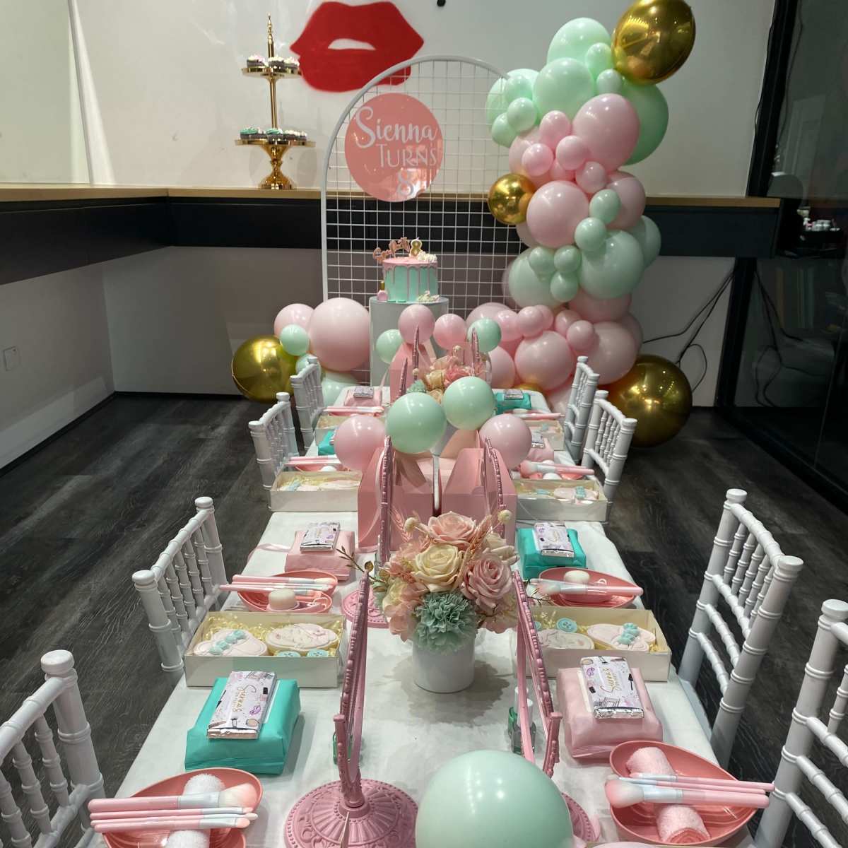 A festive table is set with pastel-colored decorations, party favors, and a backdrop featuring a lip-themed design.