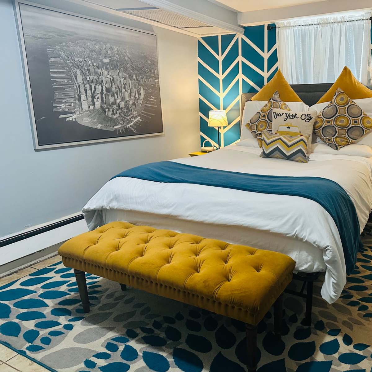 A cozy bedroom featuring a bed with decorative pillows, a yellow bench, and a geometric-patterned accent wall.