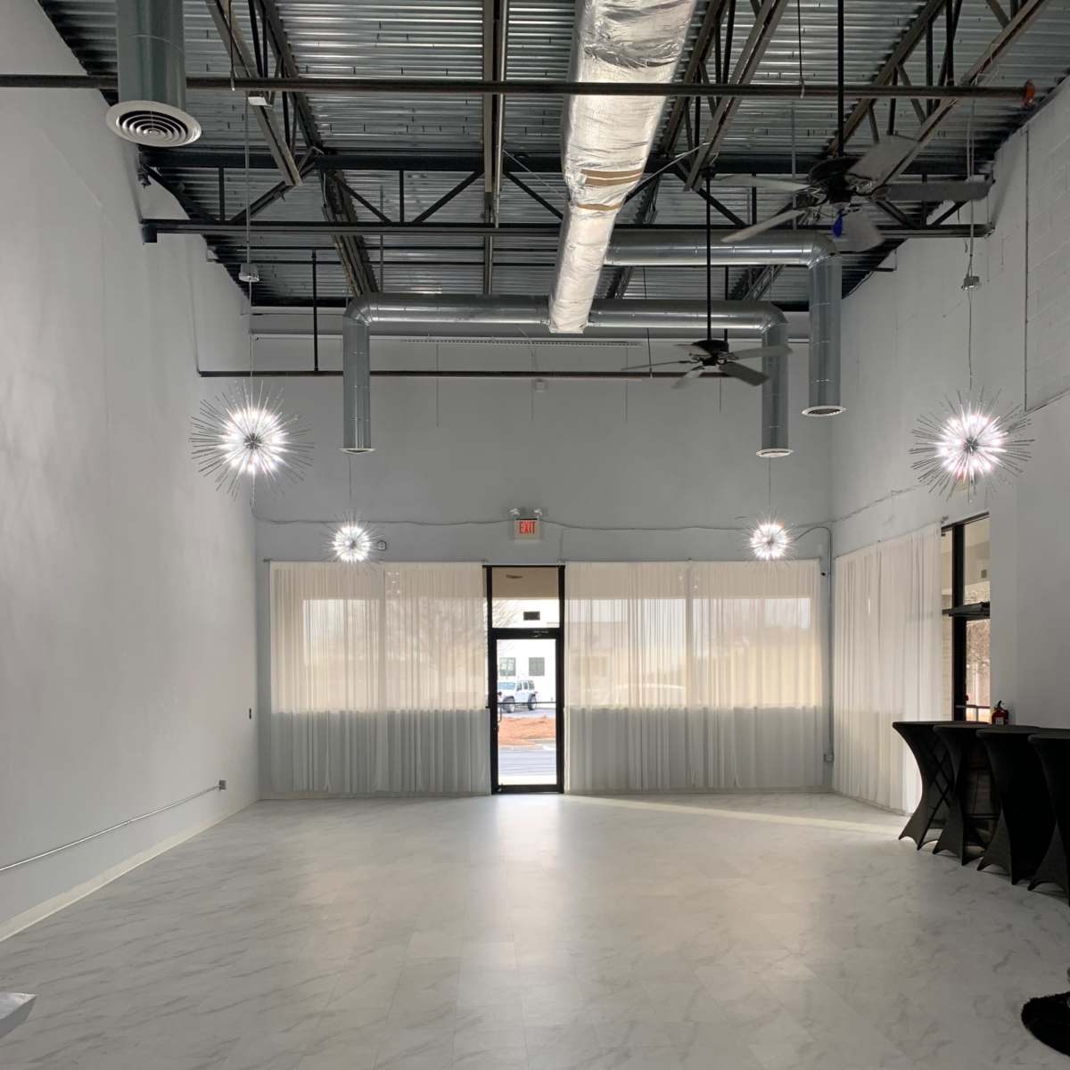 An empty, well-lit interior space with a marble-like floor, large windows, and decorative light fixtures hanging from the ceiling.