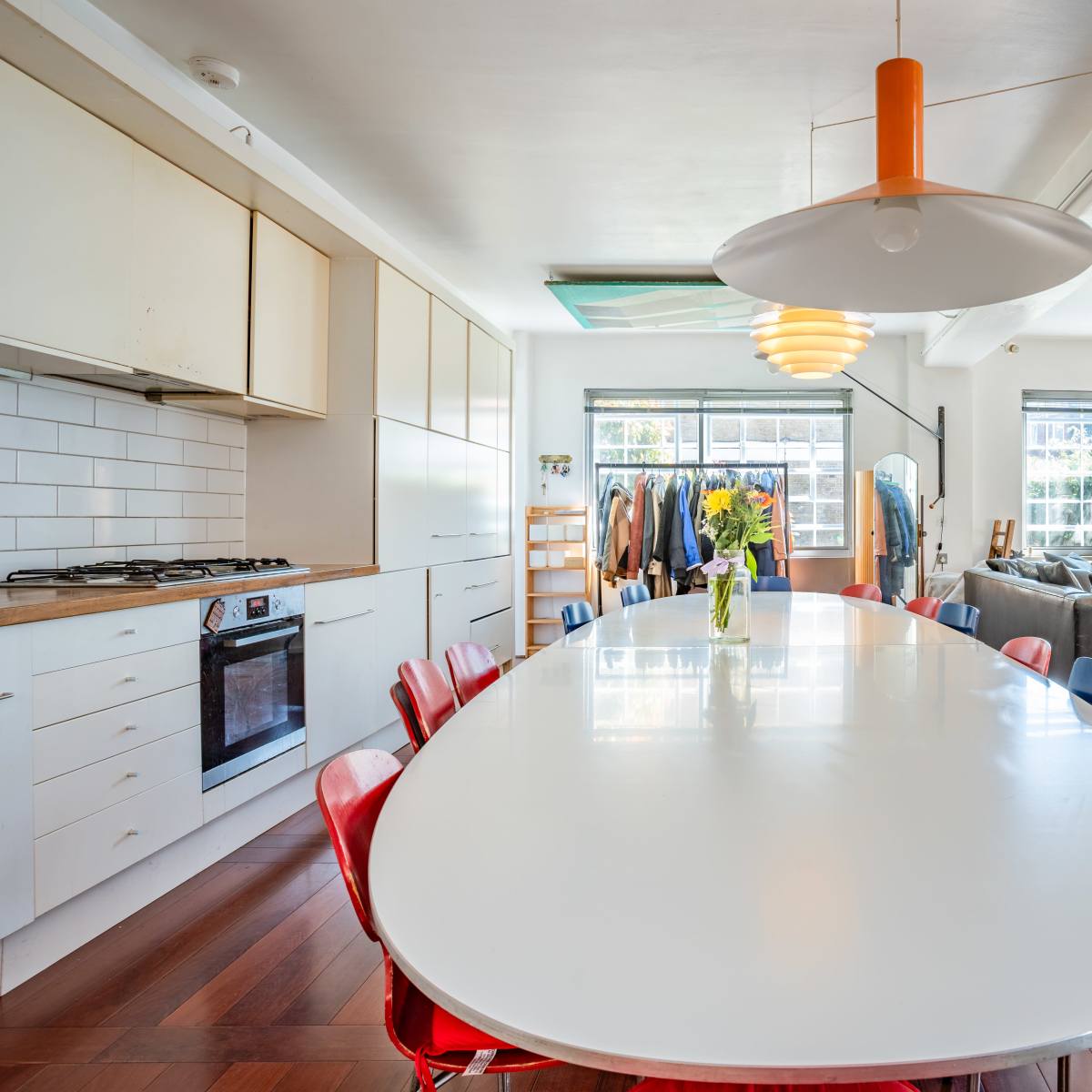A modern kitchen and dining area with a long white table surrounded by colorful chairs and large windows letting in natural light.