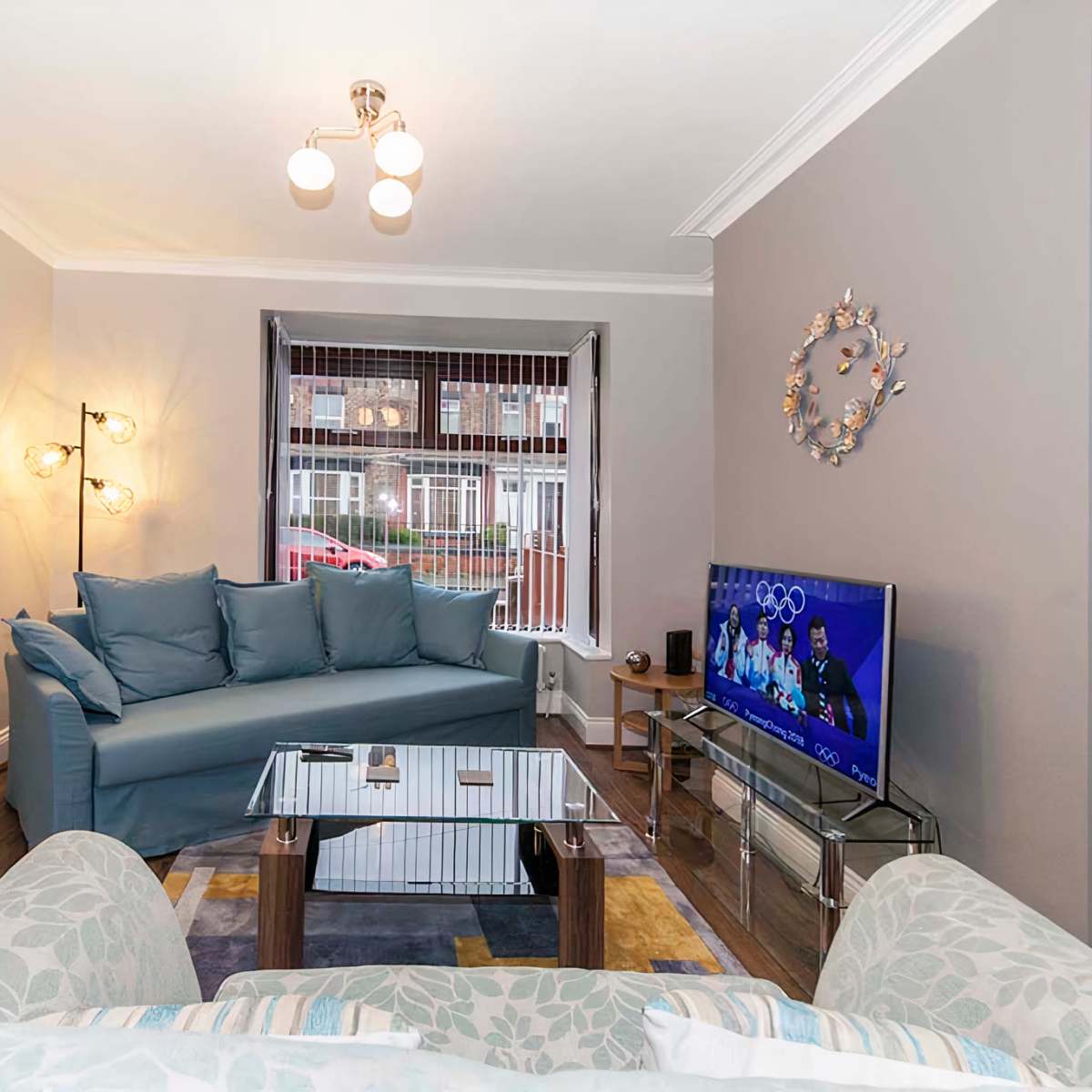 A furnished living room with a blue sofa, a glass coffee table, and a television displaying a program.