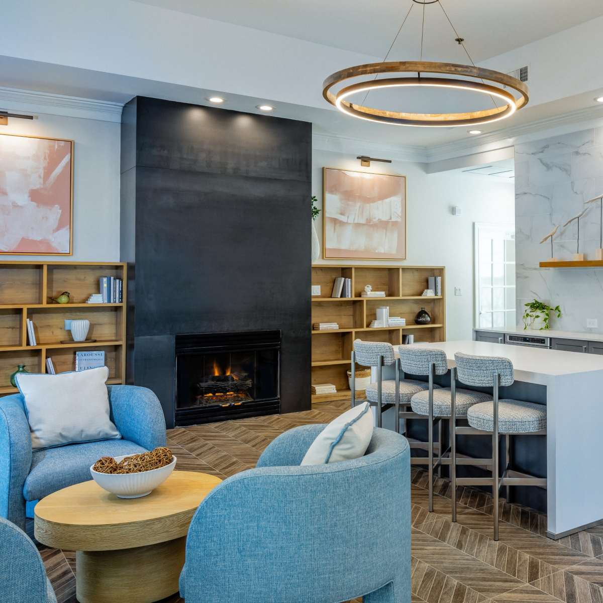 A modern living space featuring a sleek kitchen with gray cabinetry, a large island with seating, a fireplace, and a cozy seating area with light blue chairs.