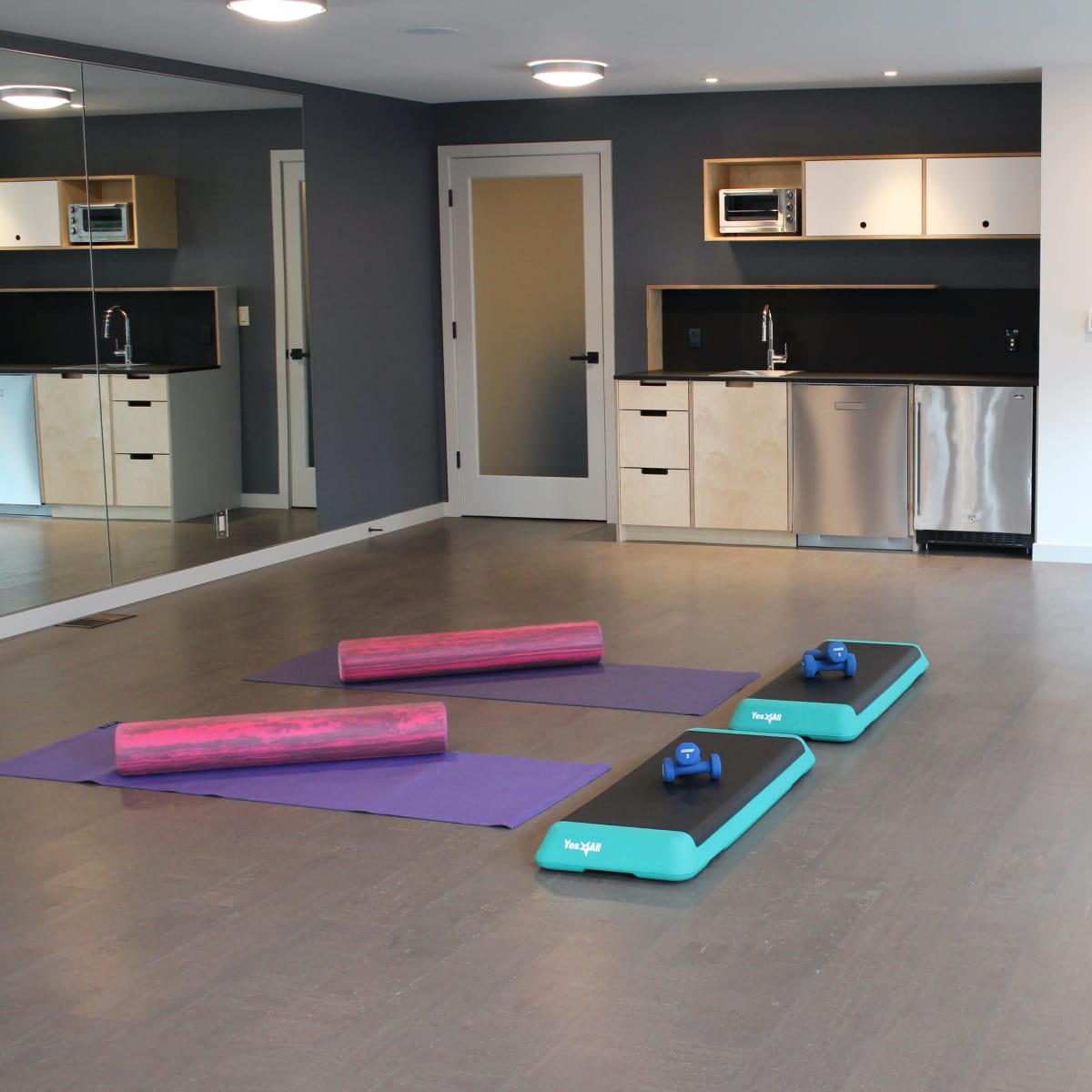 A modern fitness studio with two yoga mats, foam rollers, and a kitchenette area.