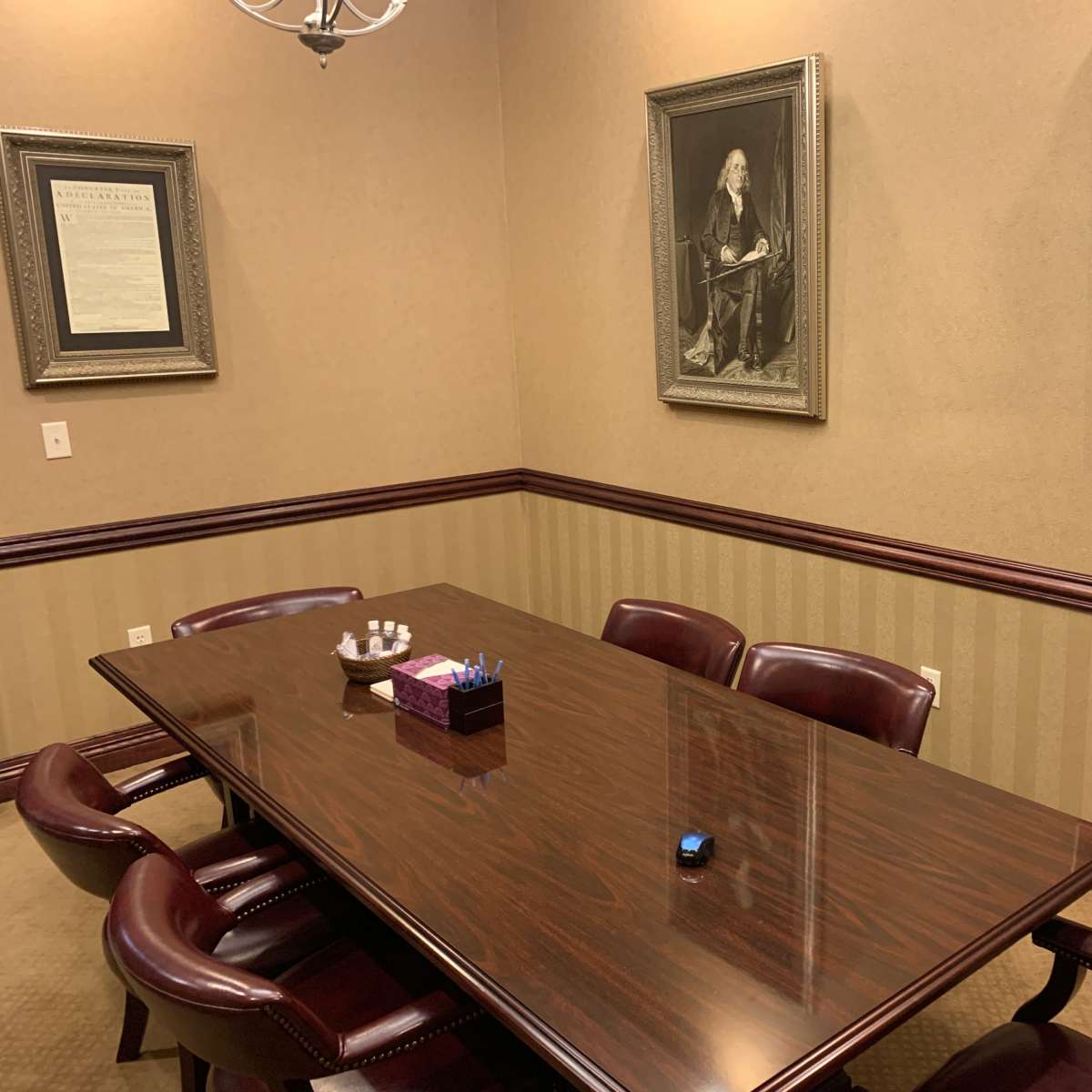 A conference room with a wooden table surrounded by leather chairs, featuring framed artwork on the walls and a decorative centerpiece on the table.