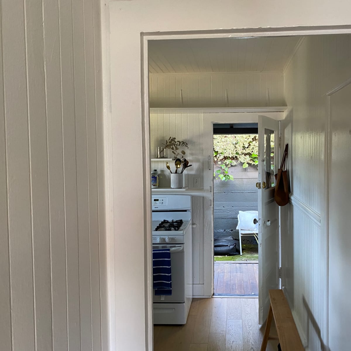 A hallway leads to a kitchen where a stove is visible, with an outdoor patio seen through an open door.