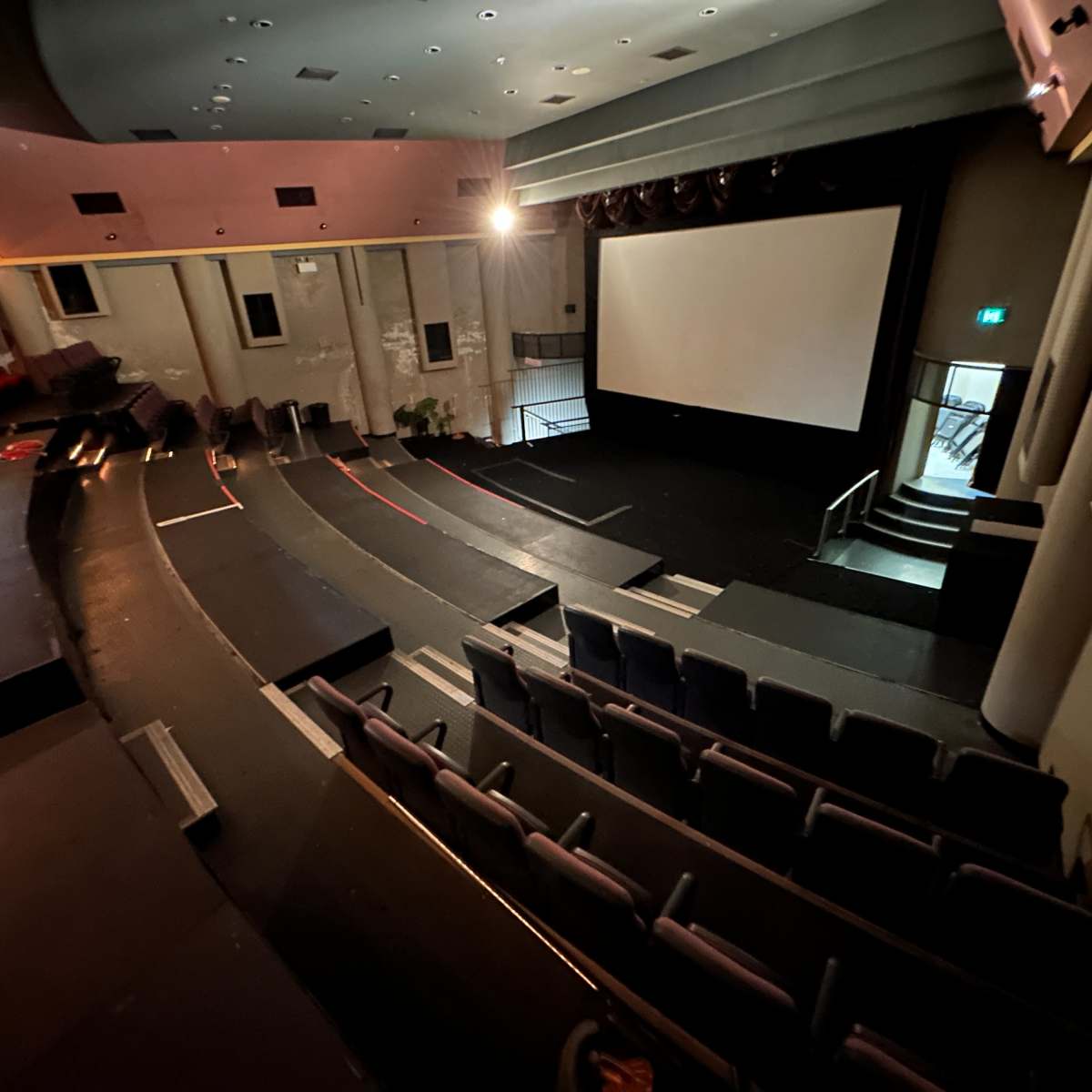 An empty auditorium with tiered seating facing a large screen, illuminated by soft lighting.