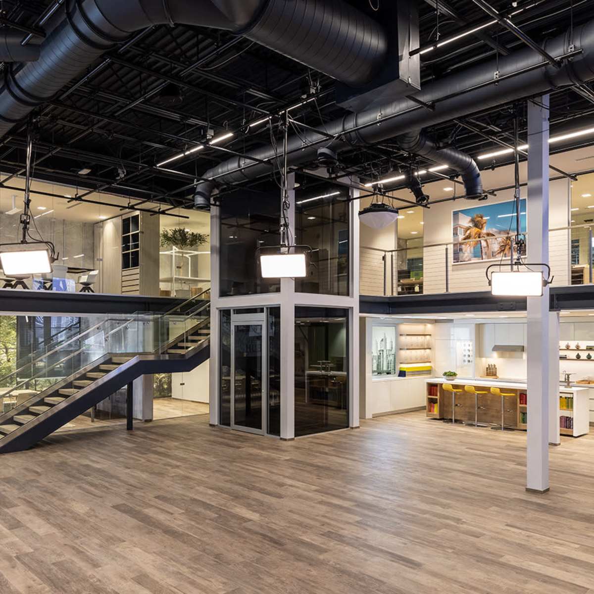 A modern office space with an open layout, featuring a staircase, glass-walled meeting rooms, and areas for collaboration and relaxation.