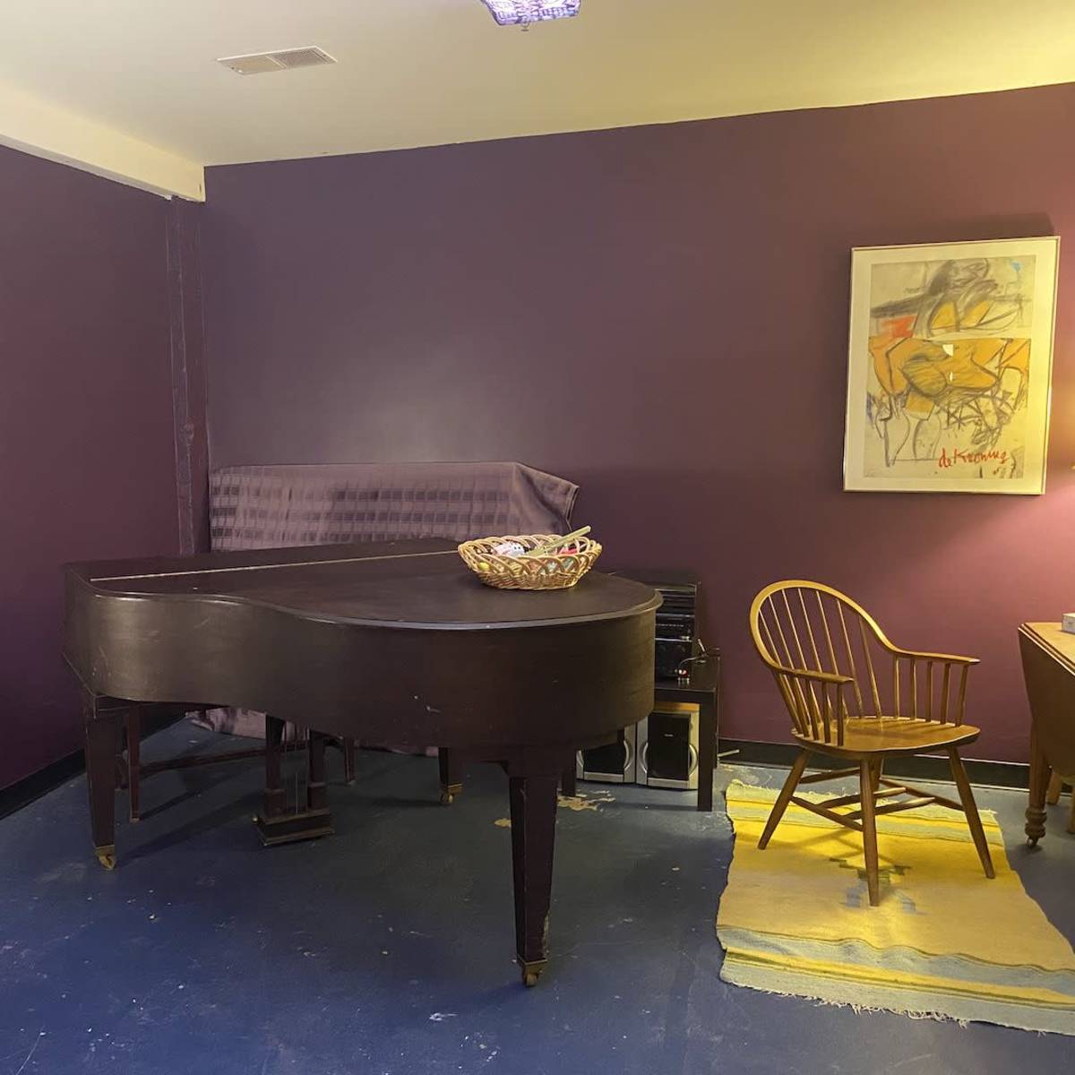 A dimly lit room featuring a grand piano, a wooden chair, and two framed artworks on purple walls.