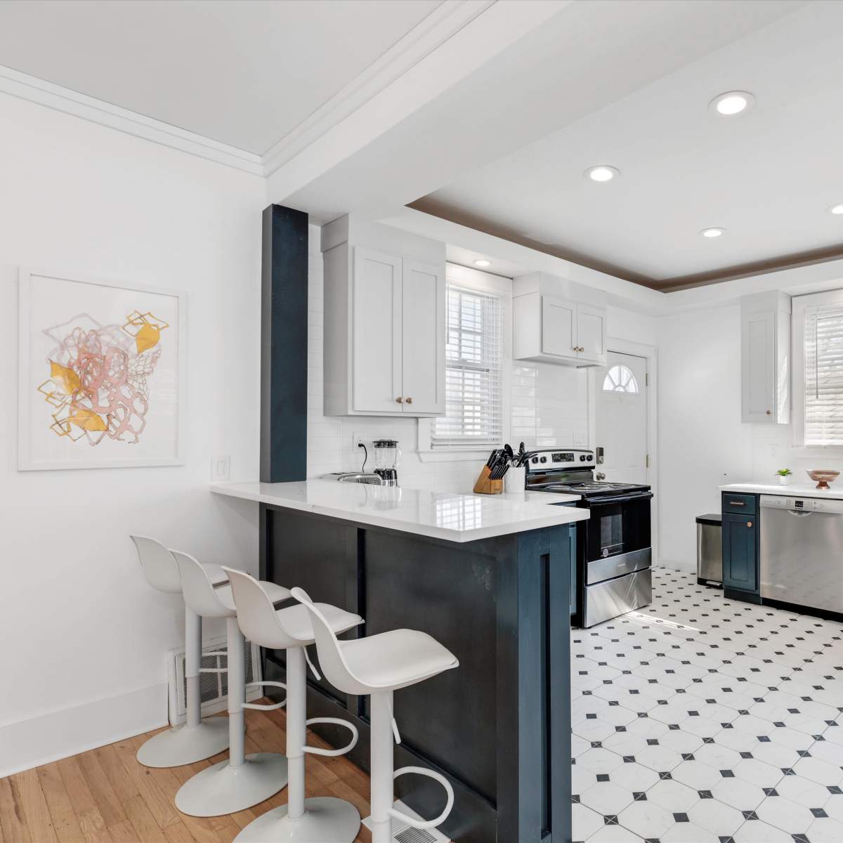A modern kitchen features white cabinetry, dark blue lower cabinets, and a black stove, with a tiled floor and bar seating.