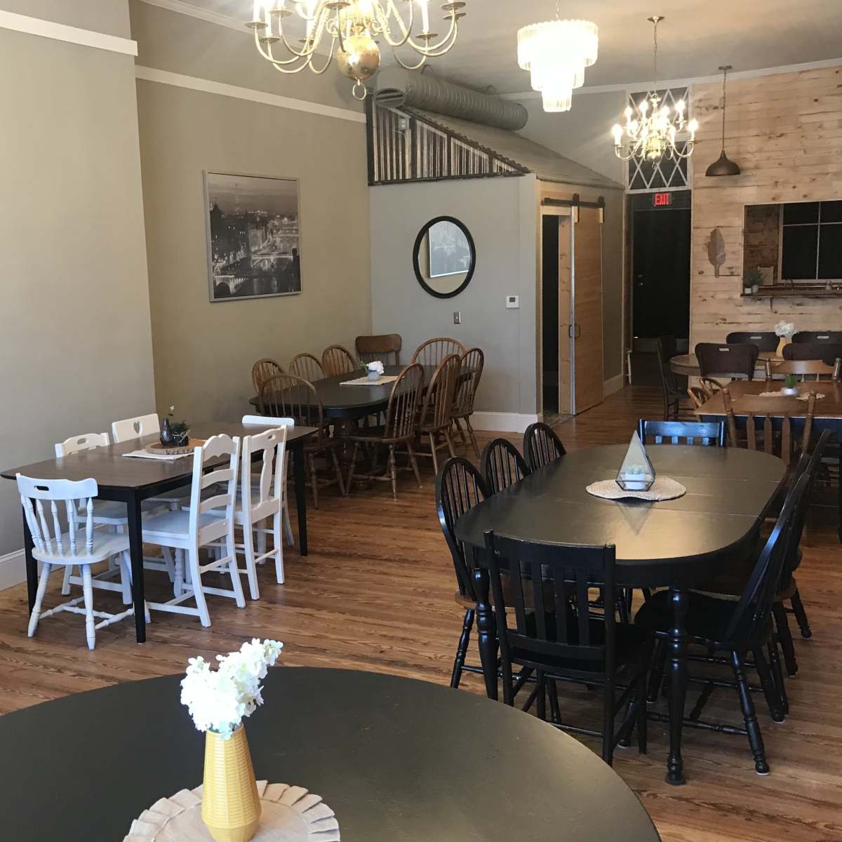 A spacious dining area with various tables and chairs arranged around the room, featuring a mix of light and dark wood finishes.