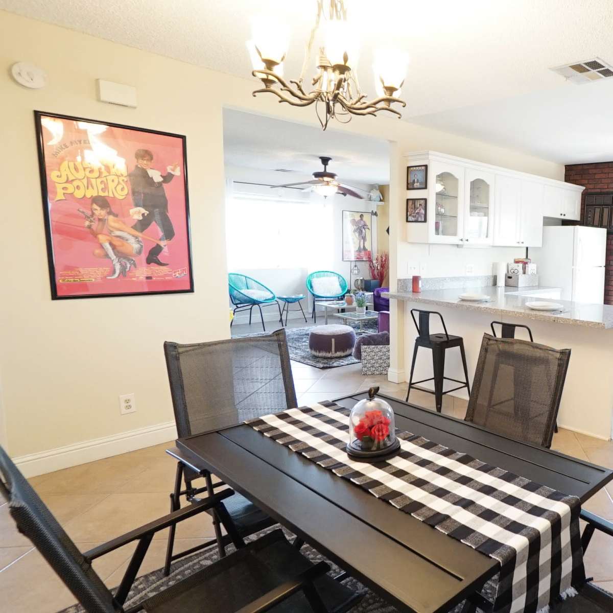 A dining area with a black table and chairs is situated next to a kitchen featuring a large window, granite countertops, and brick accent walls.