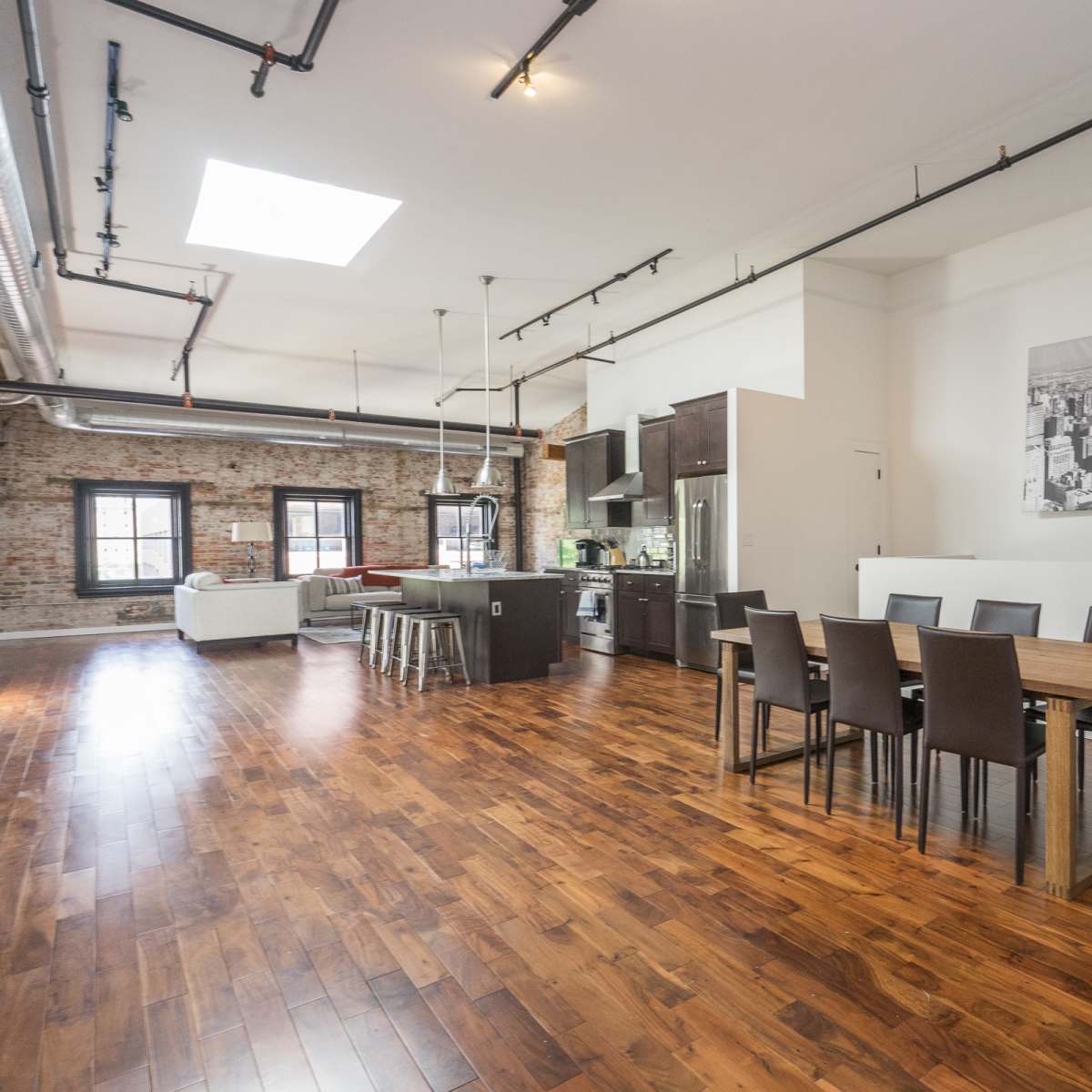 An open-concept loft with exposed brick walls, a modern kitchen, and a large dining table set for six.