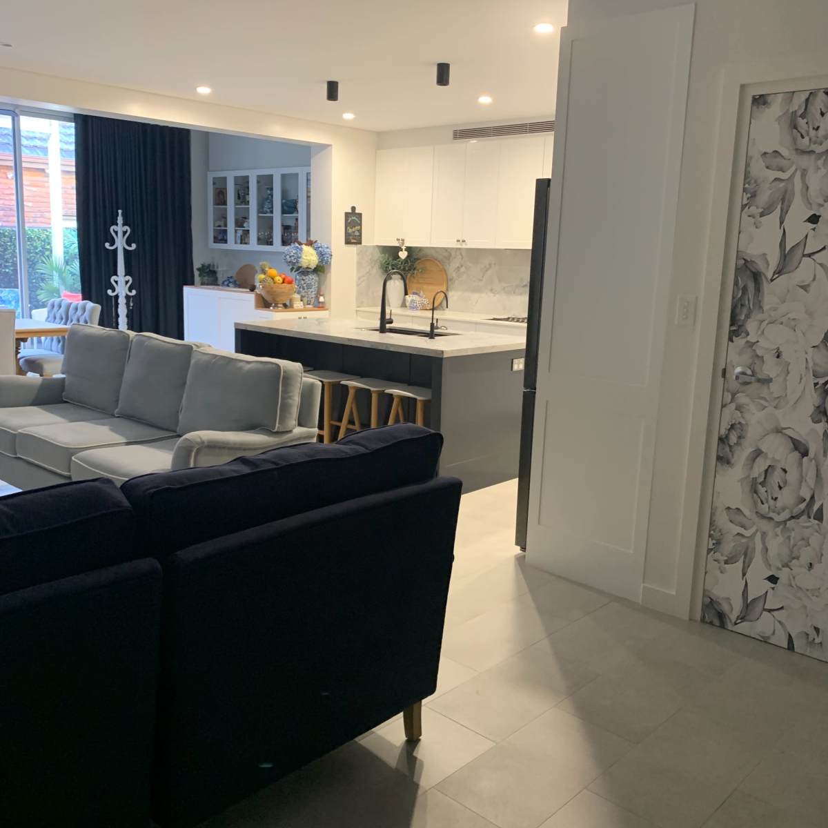 A modern open-concept living area leading into a kitchen, featuring a seating area with a sectional sofa and a dining space with bar stools.
