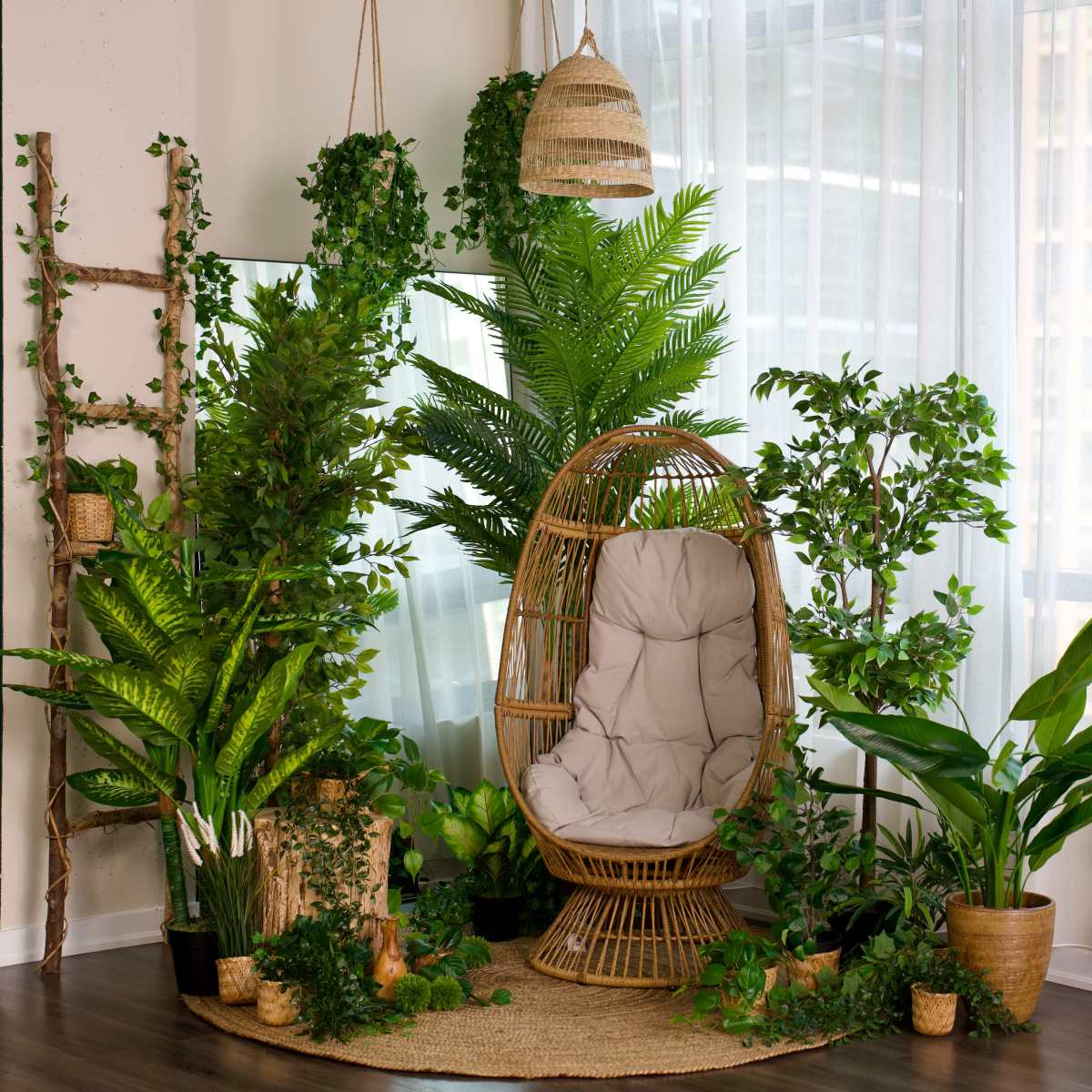 A cozy rattan hanging chair is surrounded by various indoor plants in a brightly lit room with sheer curtains.
