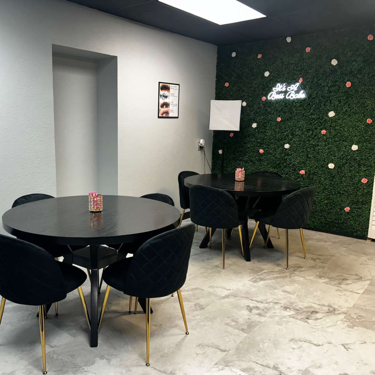 A modern interior space with two round black tables surrounded by black chairs, a green wall with decorative elements, and framed posters on the walls.