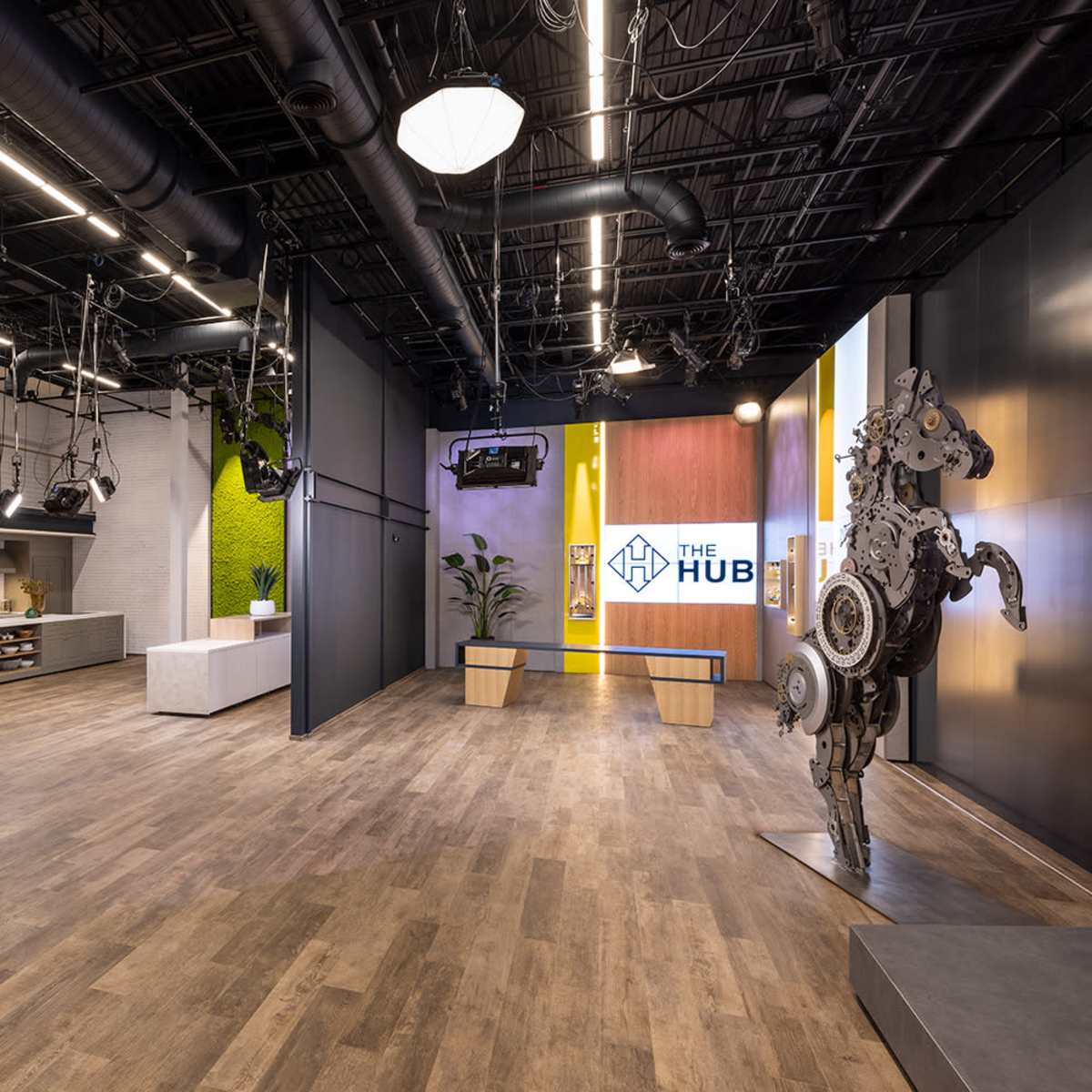 A modern, open interior space featuring wooden flooring, green moss-covered walls, and a display area with a large sign reading "THE HUB."