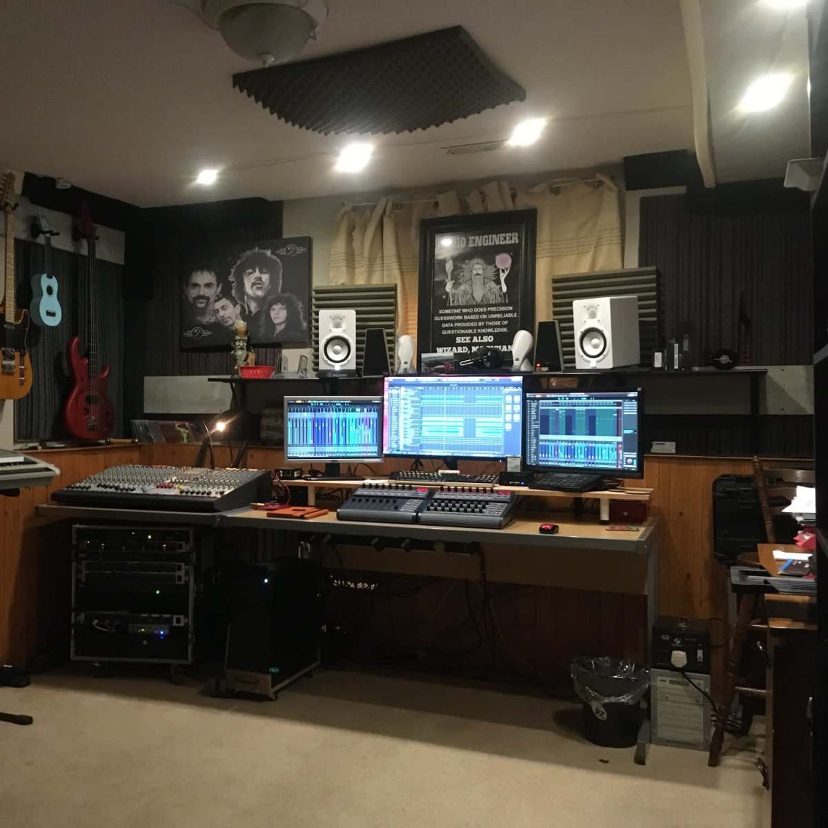 A home music studio features guitars on the walls, audio equipment, and multiple monitors displaying digital audio workstations.
