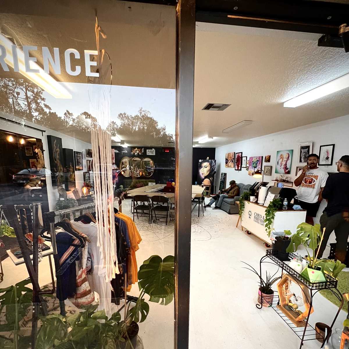 A view through a glass door into a creatively arranged indoor space featuring clothing displays, art on the walls, and tables set up for an event.