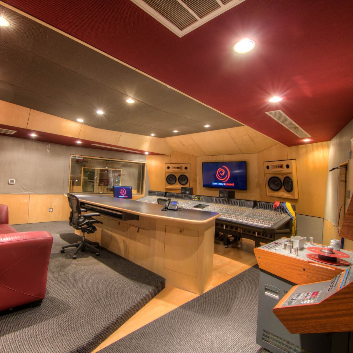 A modern recording studio with a large mixing console, a comfortable red sofa, and soundproof walls.