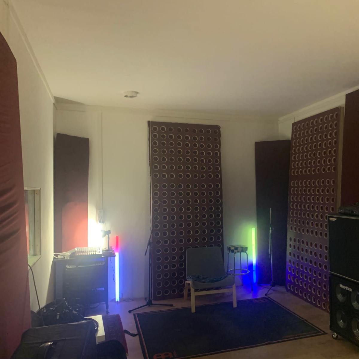 A soundproofed music studio with acoustic panels, a chair, and audio equipment illuminated by colorful lights.