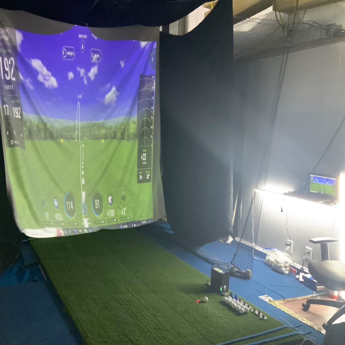An indoor golf simulator setup with a large screen displaying golf course graphics and a synthetic turf mat.