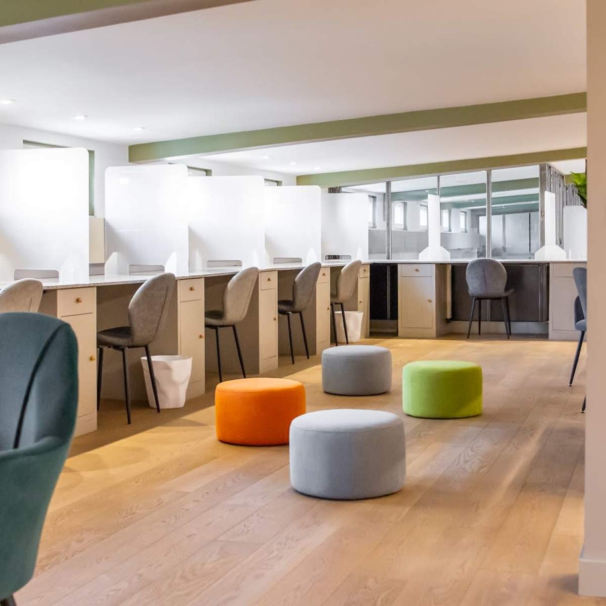 A modern office space with multiple workstations, colorfully upholstered stools, and a streamlined design.